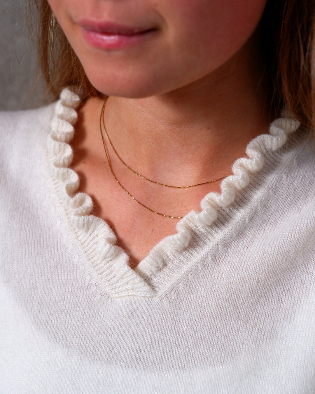 Nærbillede af flæsedetaljer ved halsudskæring, Oyu cashmere bluse i Natural white.