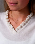Nærbillede af flæsedetaljer ved halsudskæring, Oyu cashmere bluse i Natural white.