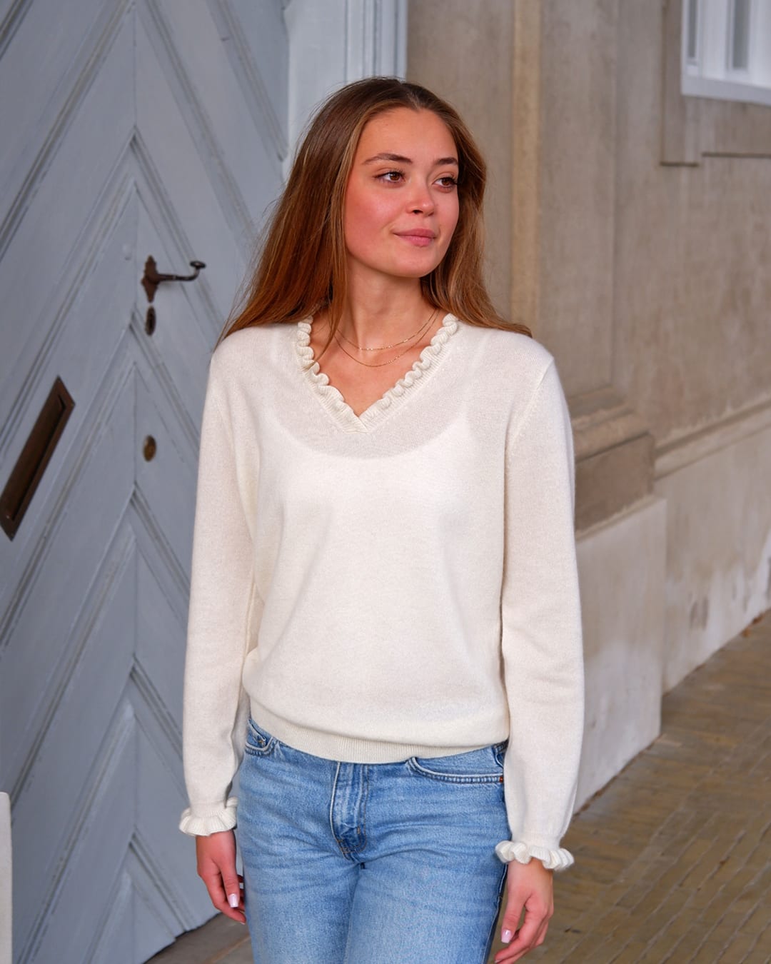 Kvinde iført cashmere bluse i Natural white med flæsedetaljer ved halsudskæring.