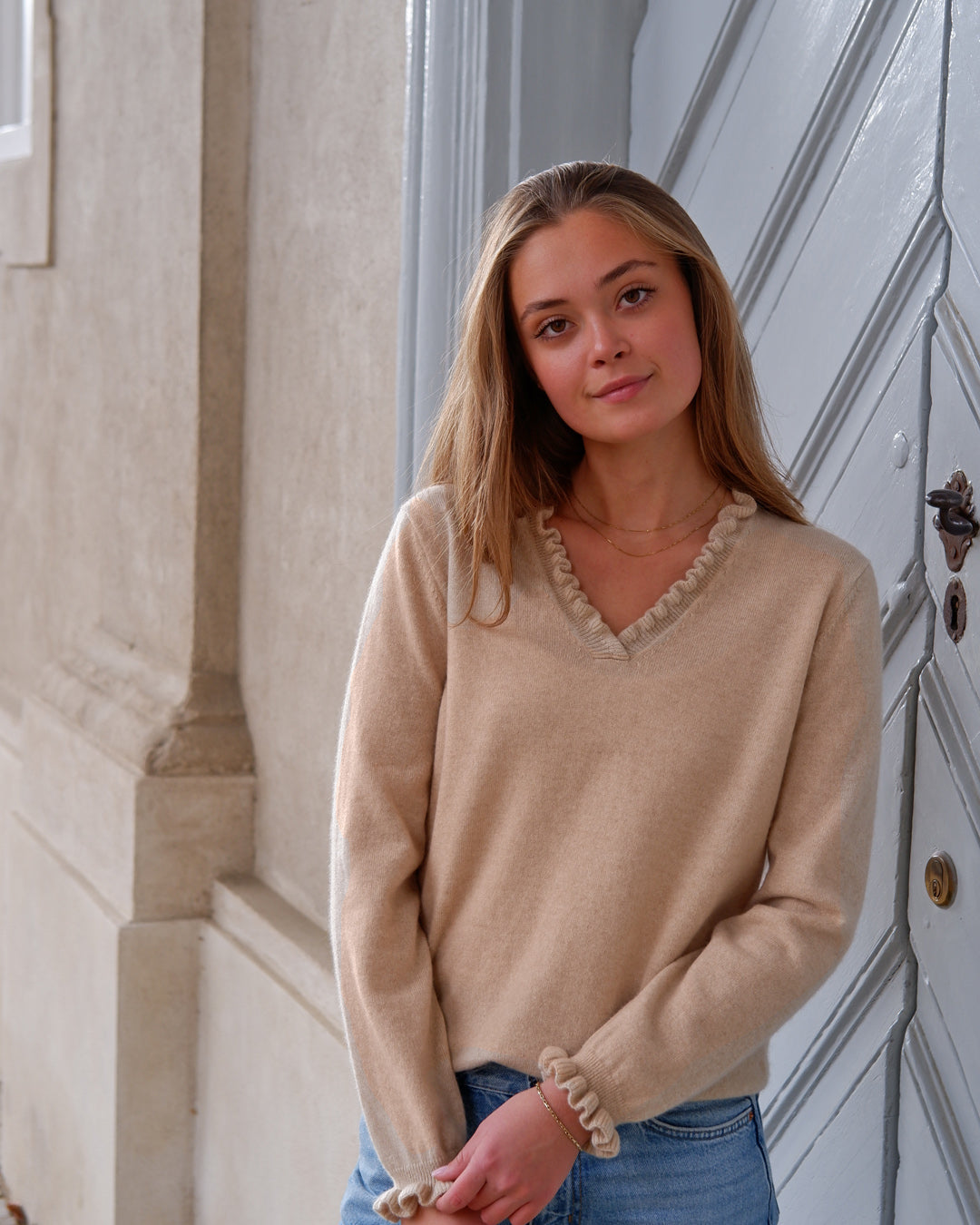 Kvinde iført cashmere bluse i Natural sand med flæsedetaljer ved halsudskæring.