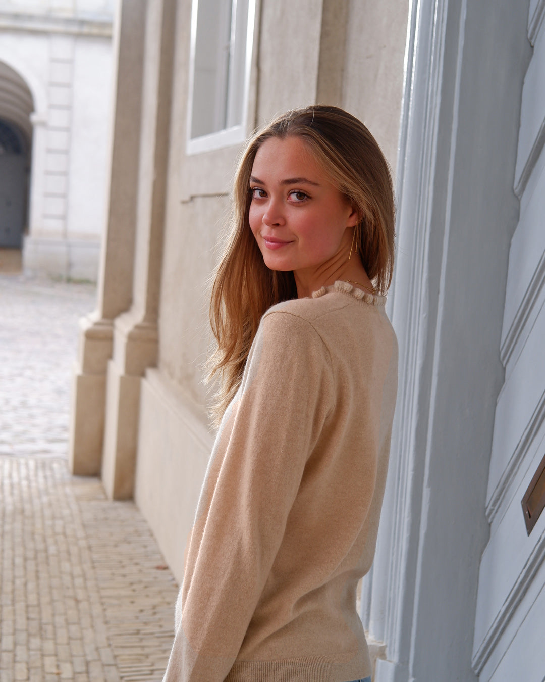 Kvinde iført cashmere bluse i Natural sand med flæsedetaljer ved halsudskæring, set bagfra.