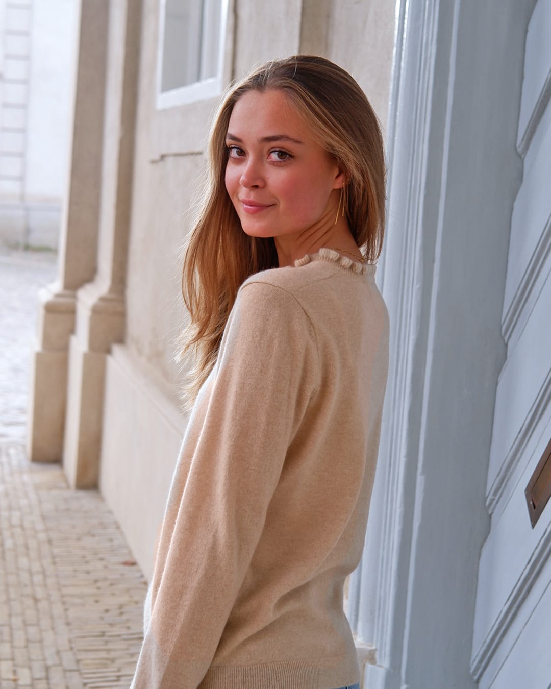 Kvinde iført cashmere bluse i Natural sand med flæsedetaljer ved halsudskæring, set bagfra.