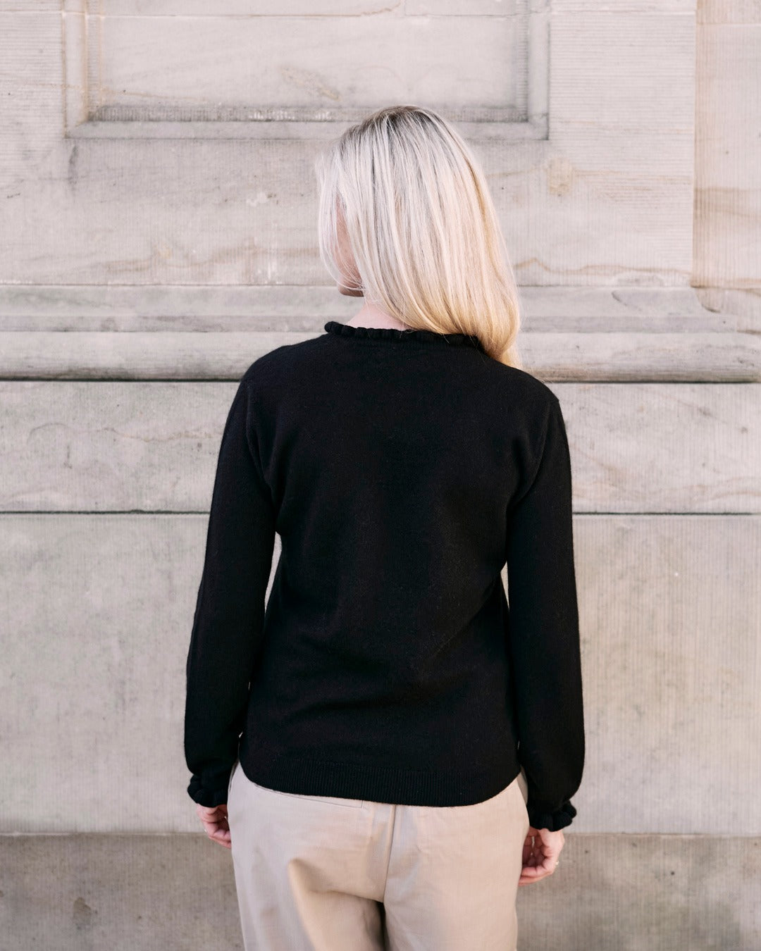 Kvinde iført cashmere bluse i Black med flæsedetaljer ved halsudskæring, set bagfra.