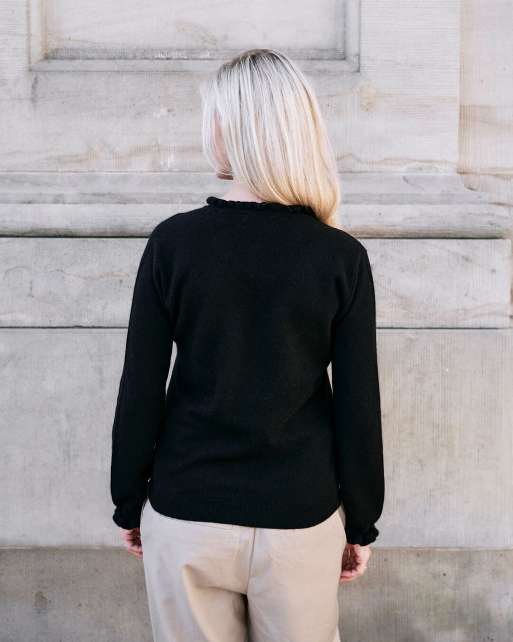 Kvinde iført cashmere bluse i Black med flæsedetaljer ved halsudskæring, set bagfra.