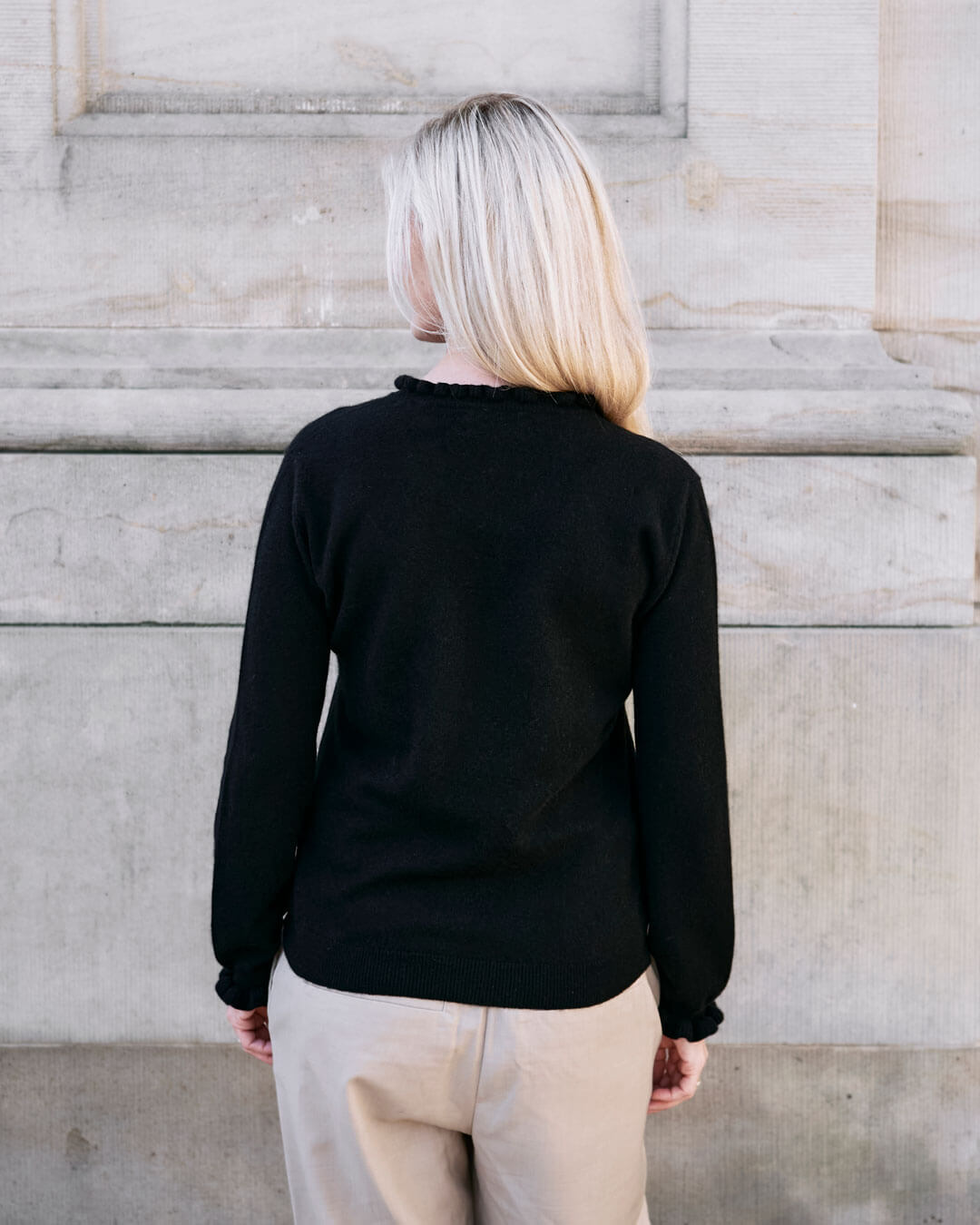 Kvinde iført cashmere bluse i Black med flæsedetaljer ved halsudskæring, set bagfra.