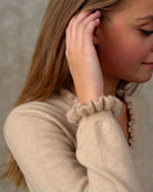 Nærbillede af flæsedetaljer på ærme og halsudskæring, Oyu cashmere bluse i Natural sand.