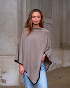 Kvinde iført cashmere poncho Sarnai i Natural taupe med sort kontrastkant.