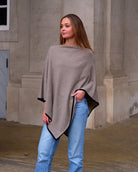 Cashmere poncho Sarnai i Natural taupe, med hånd i lomme og sort kontrastkant.