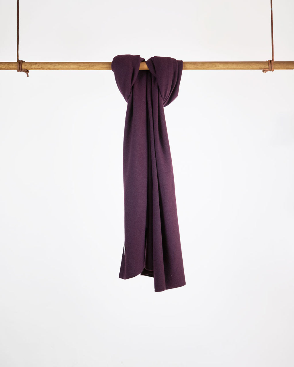 Tørklæde i cashmere, plum purple, hængende på stang mod hvid baggrund.