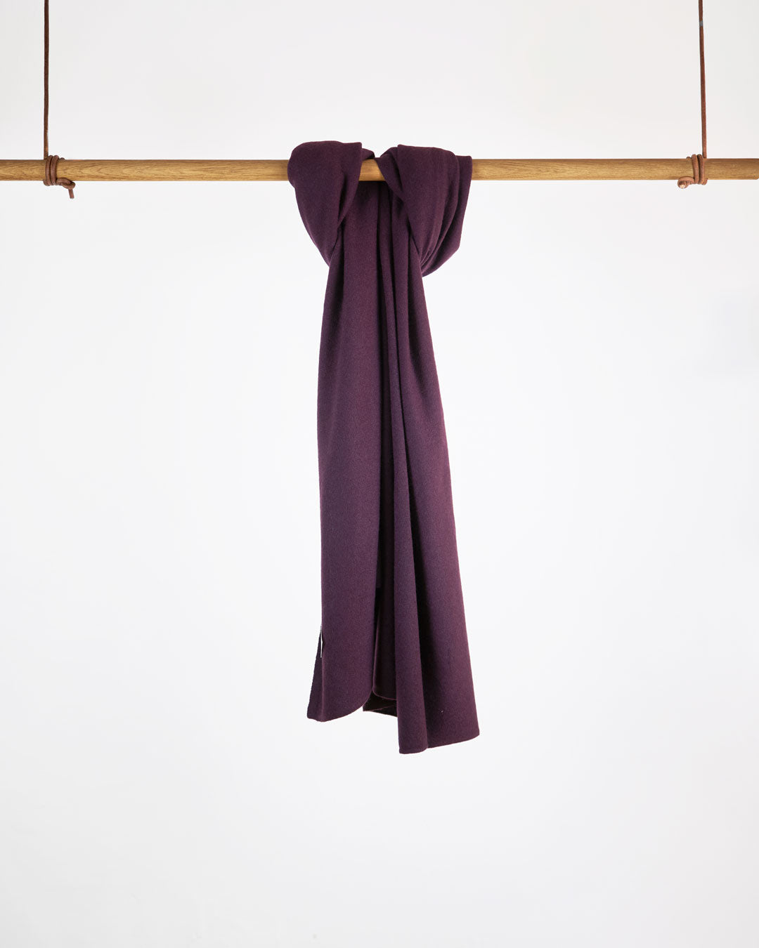 Tørklæde i cashmere, plum purple, hængende på stang mod hvid baggrund.