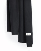 Det store tætstrikkede cashmere tørklæde i sort hænger løst.