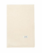 Det store naturfarvede cashmere tørklæde i lys beige ligger fladt.