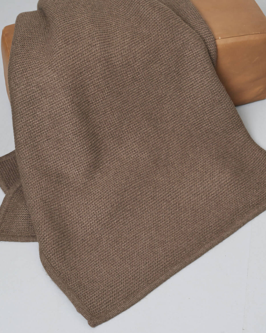 Strikket yakuld plaid i brun draperet over en puf.