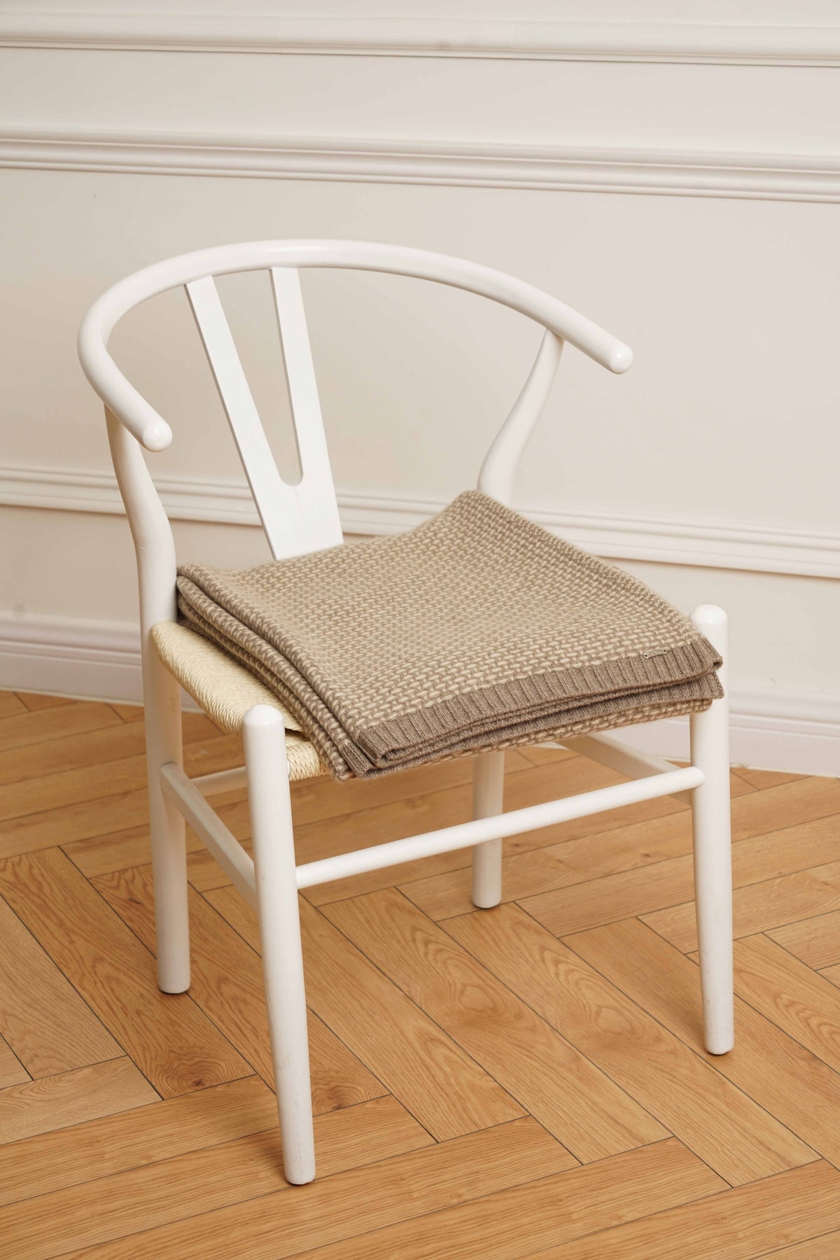 Taiga cashmere plaid i natural taupe og natural sand, foldet på en hvid stol.