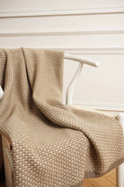 Taiga cashmere plaid i natural taupe og natural sand, draperet over en hvid stol.