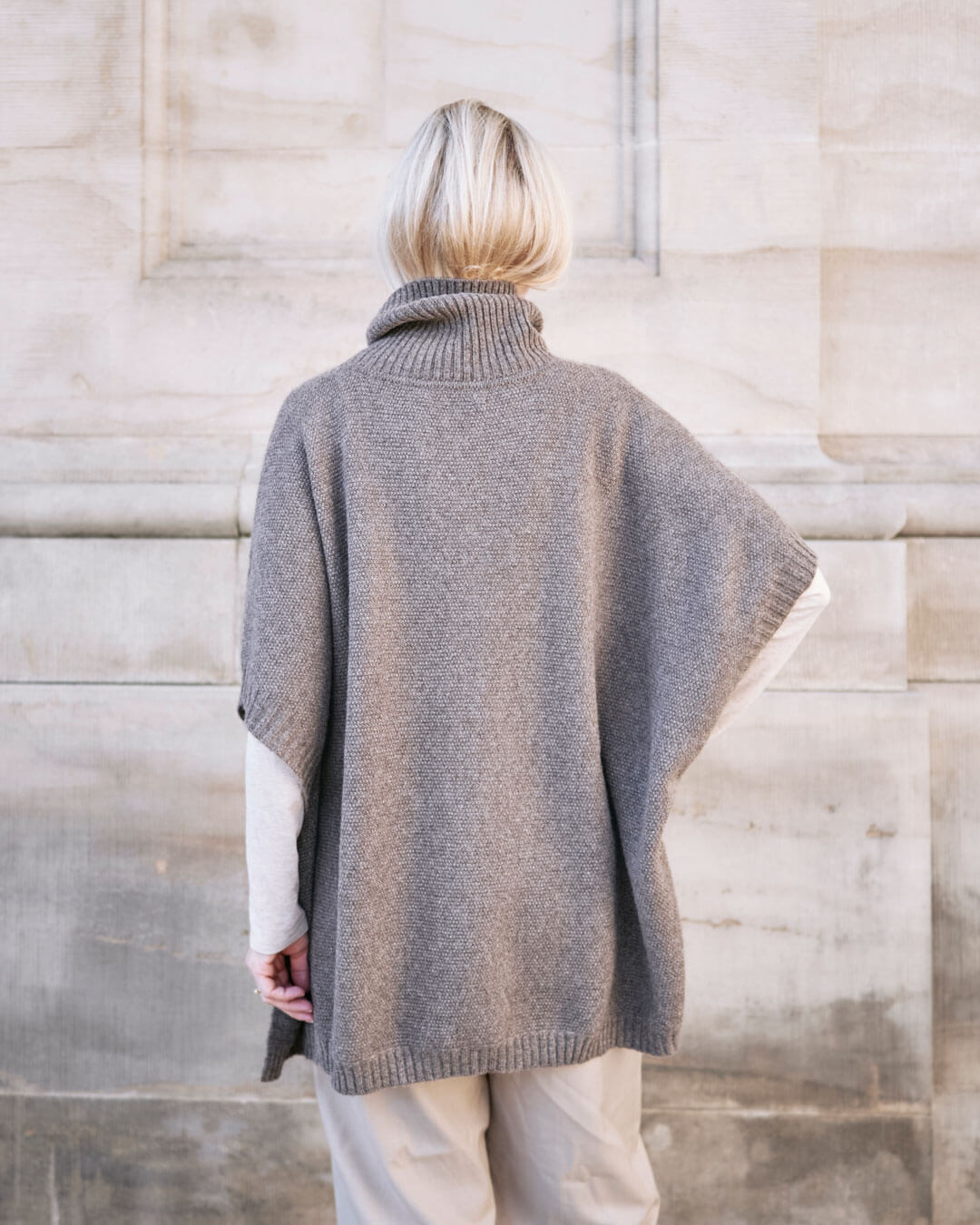 Model bære Tara yakuld poncho med rullekrave i Yak Dark Grey set bagfra.