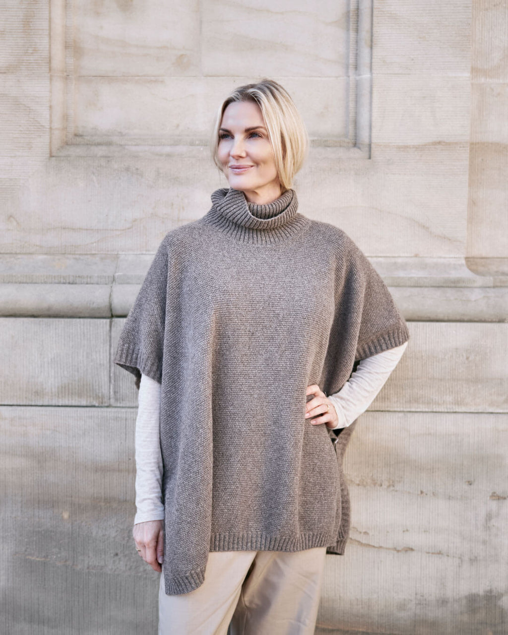 Model bærer Tara yakuld poncho med rullekrave i Yak Dark Grey.