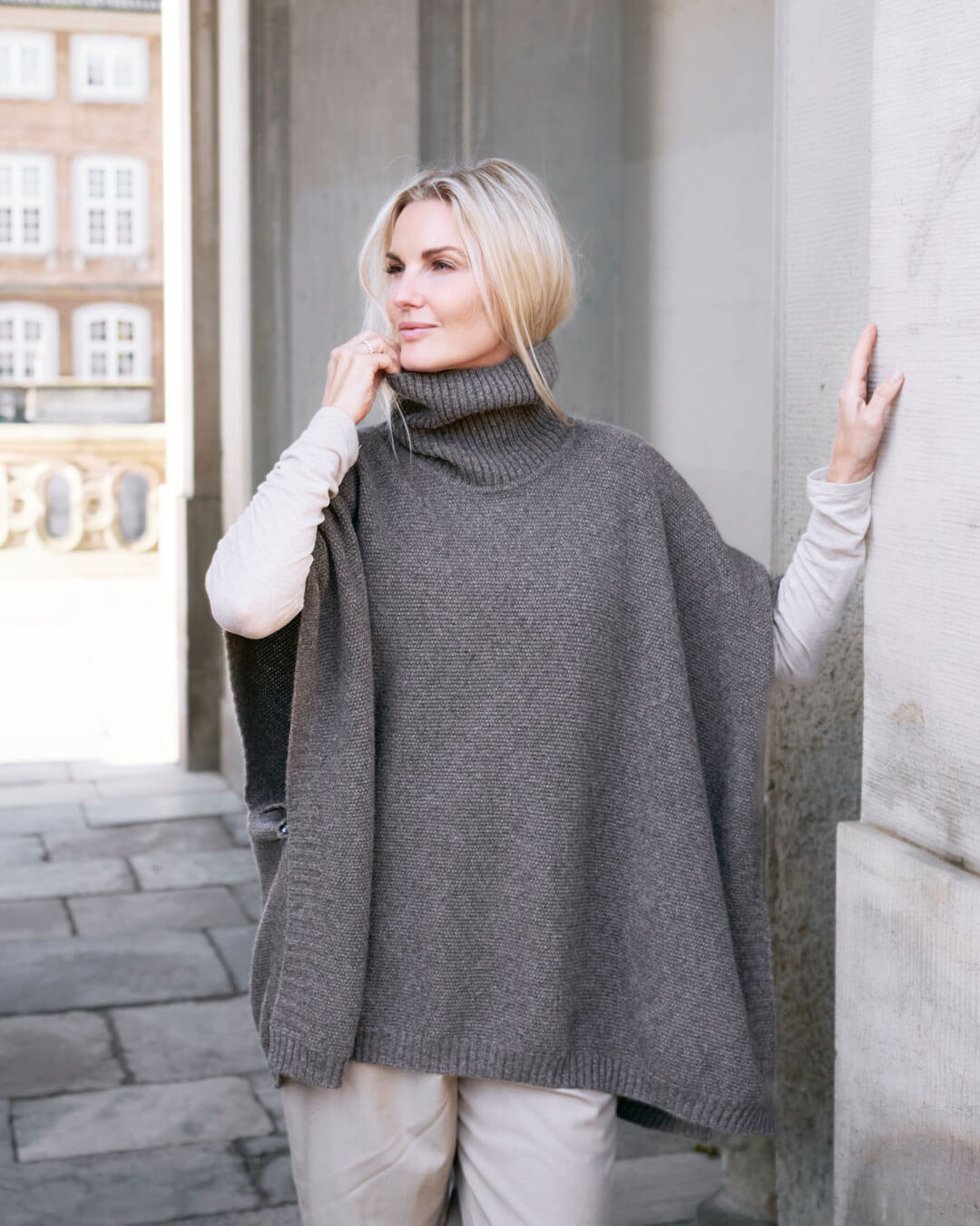 Model ved portal iført Tara yakuld poncho med rullekrave.