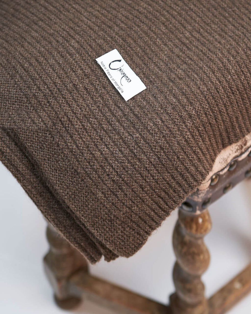 Strikket plaid i 100% yakuld i farven Yak Mocha liggende på en skammel.