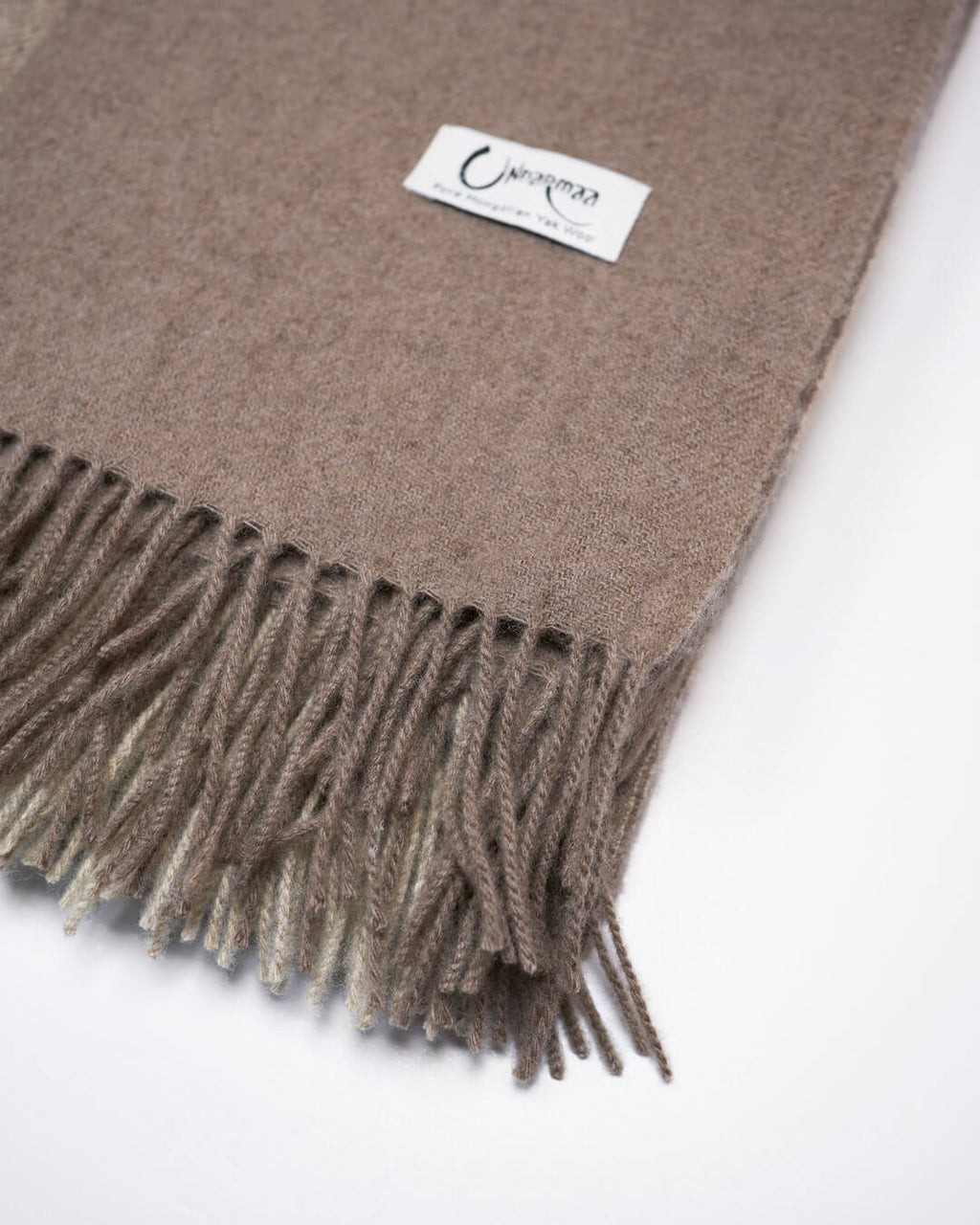 Detalje med logo fra vævet plaid i 100% yakuld med naturlige tern i beige og brun.