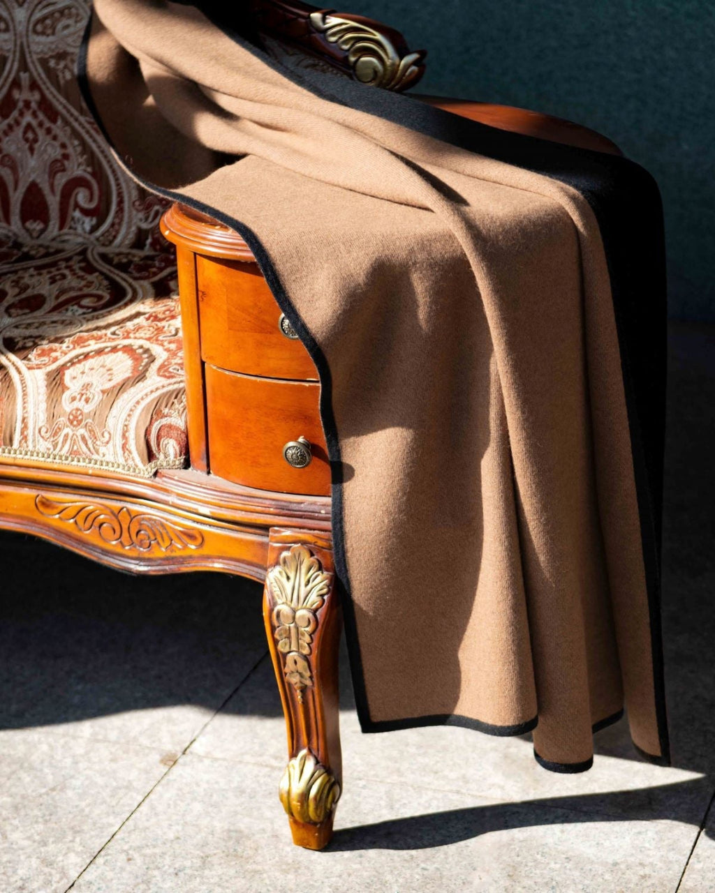 Plaid draperet over en sofa, der viser siden med den naturlige brune kameluldfarve, samtidig med, at man ser en kant af den sorte yakuld.