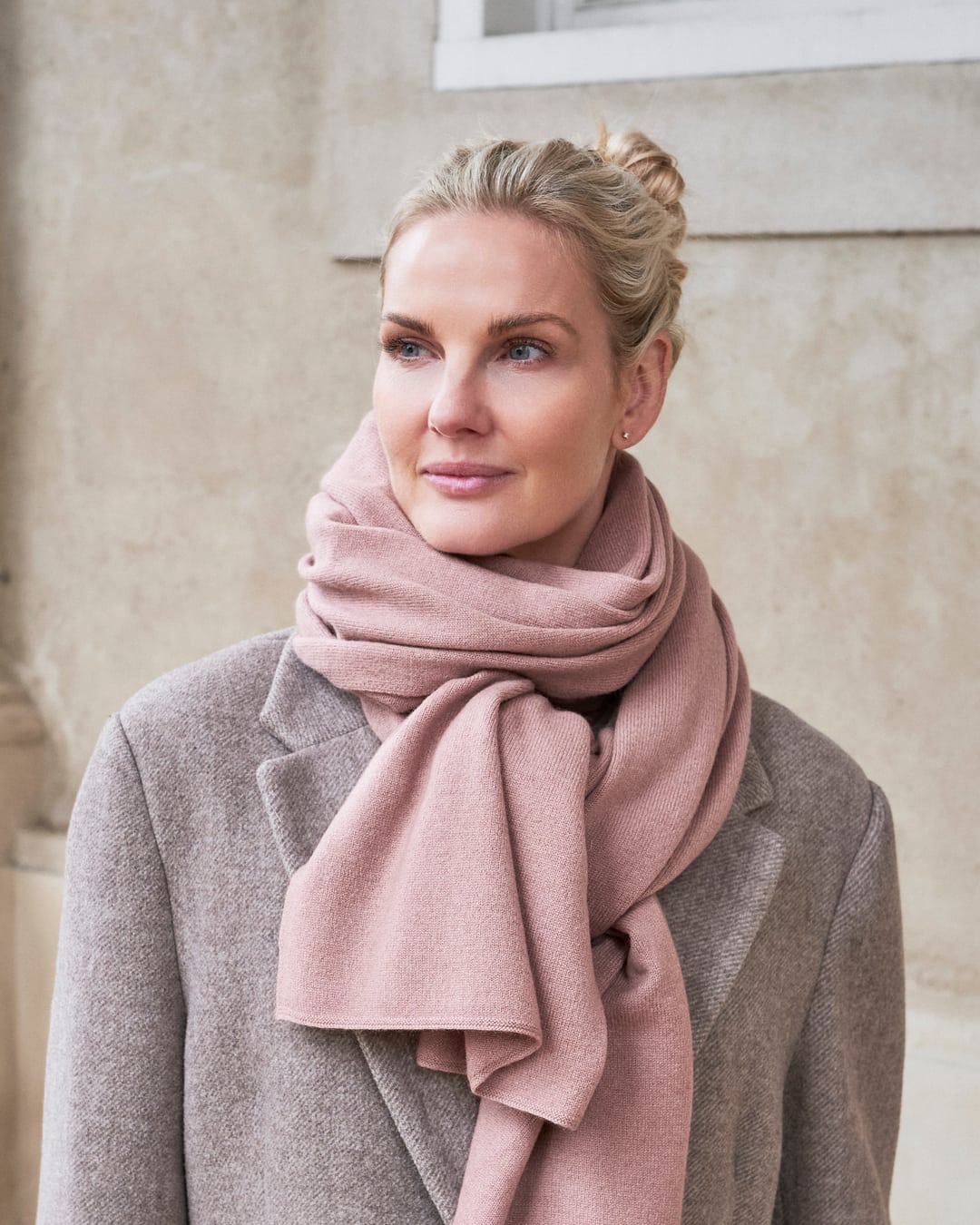 Kvinde iført cashmere tørklæde Yargui i Dusty pink, viklet løst om halsen over en frakke.