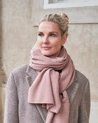 Kvinde iført cashmere tørklæde Yargui i Dusty pink, viklet løst om halsen over en frakke.