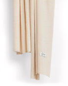 Det store cashmere tørklæde, her i naturfarvet lys beige hænger løst ned.
