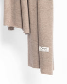 Det store cashmere tørklæde, her i naturfarvet mørk gråbeige hænger løst ned.