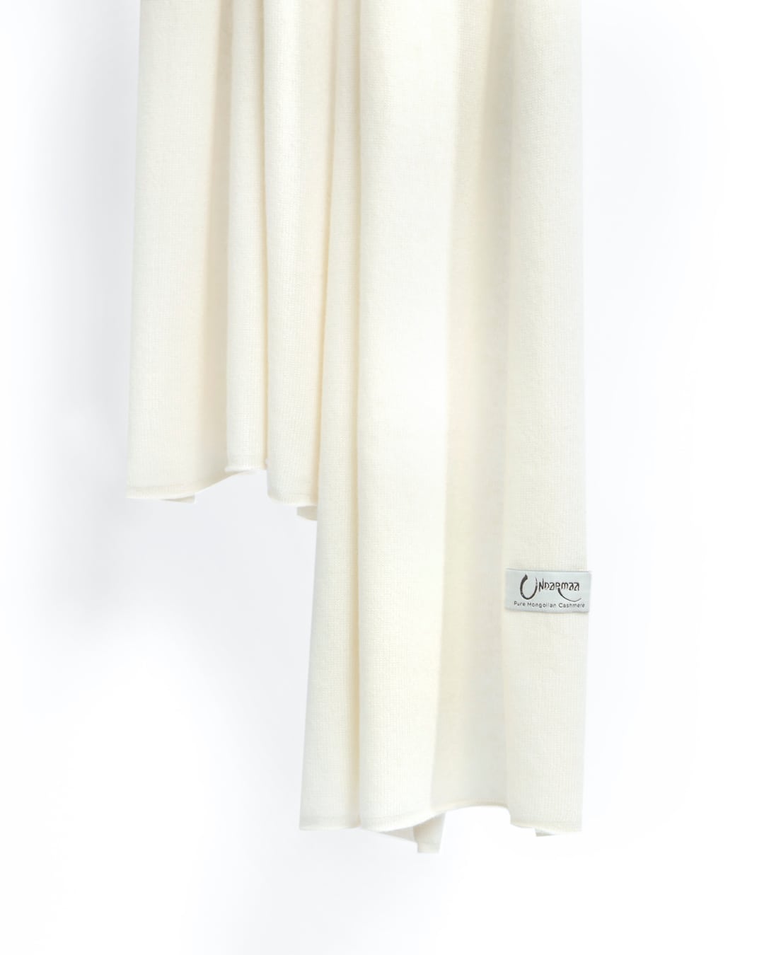Det store cashmere tørklæde, her i naturfarvet hvid hænger løst ned.