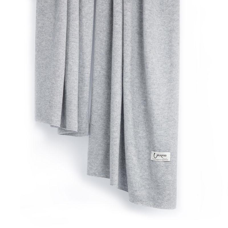 Det store tætstrikkede cashmere tørklæde i lys grå hænger løst.