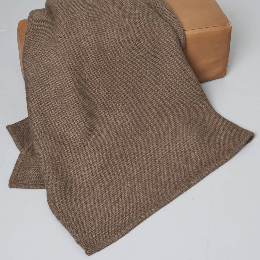 Strikket yakuld plaid i brun draperet over en puf.