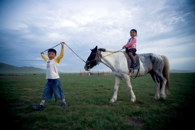 Foto fra bogen "Stemmer fra steppen", der viser børn, der rider hest og leger på steppen.